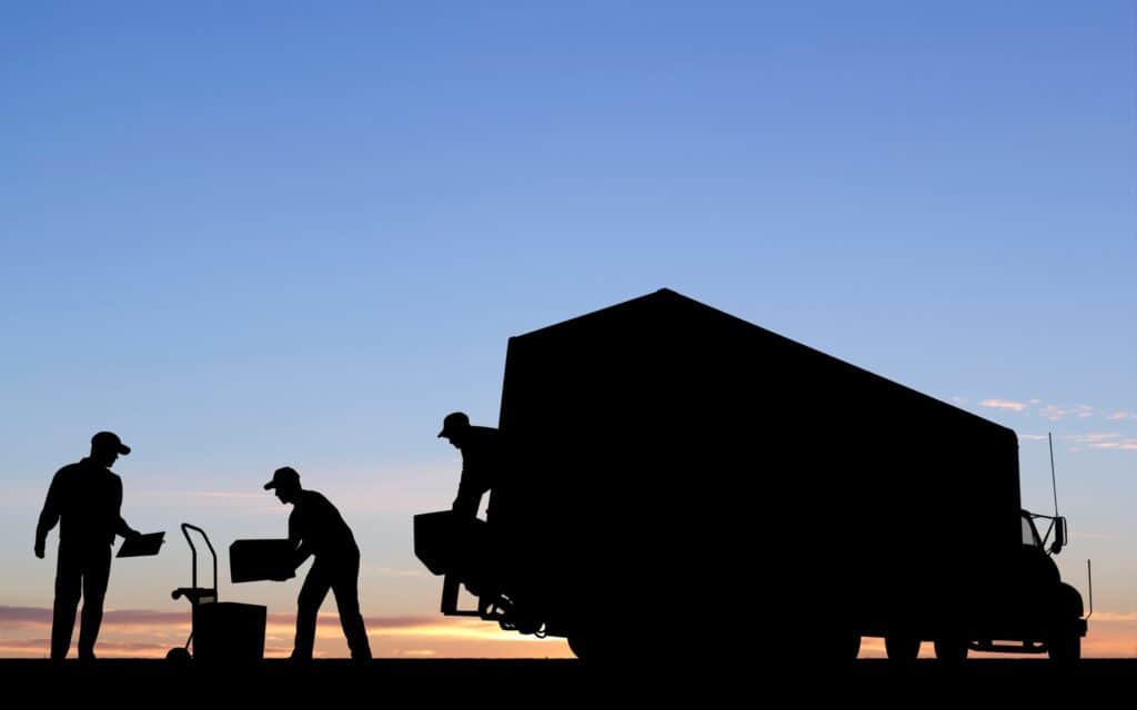 Silhouette of three people unloading boxes from a large Déménagement Économique in Montréal truck at sunset, with a clear sky in the background.