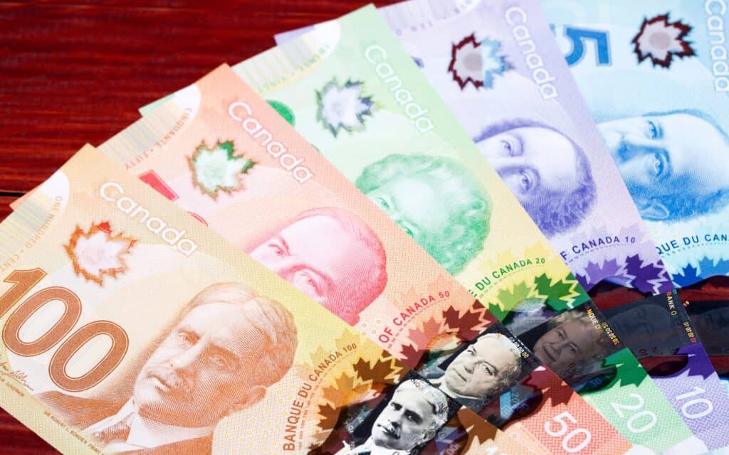 A spread of Canadian banknotes in denominations of 5, 10, 20, 50, and 100 dollars displayed on a red surface.